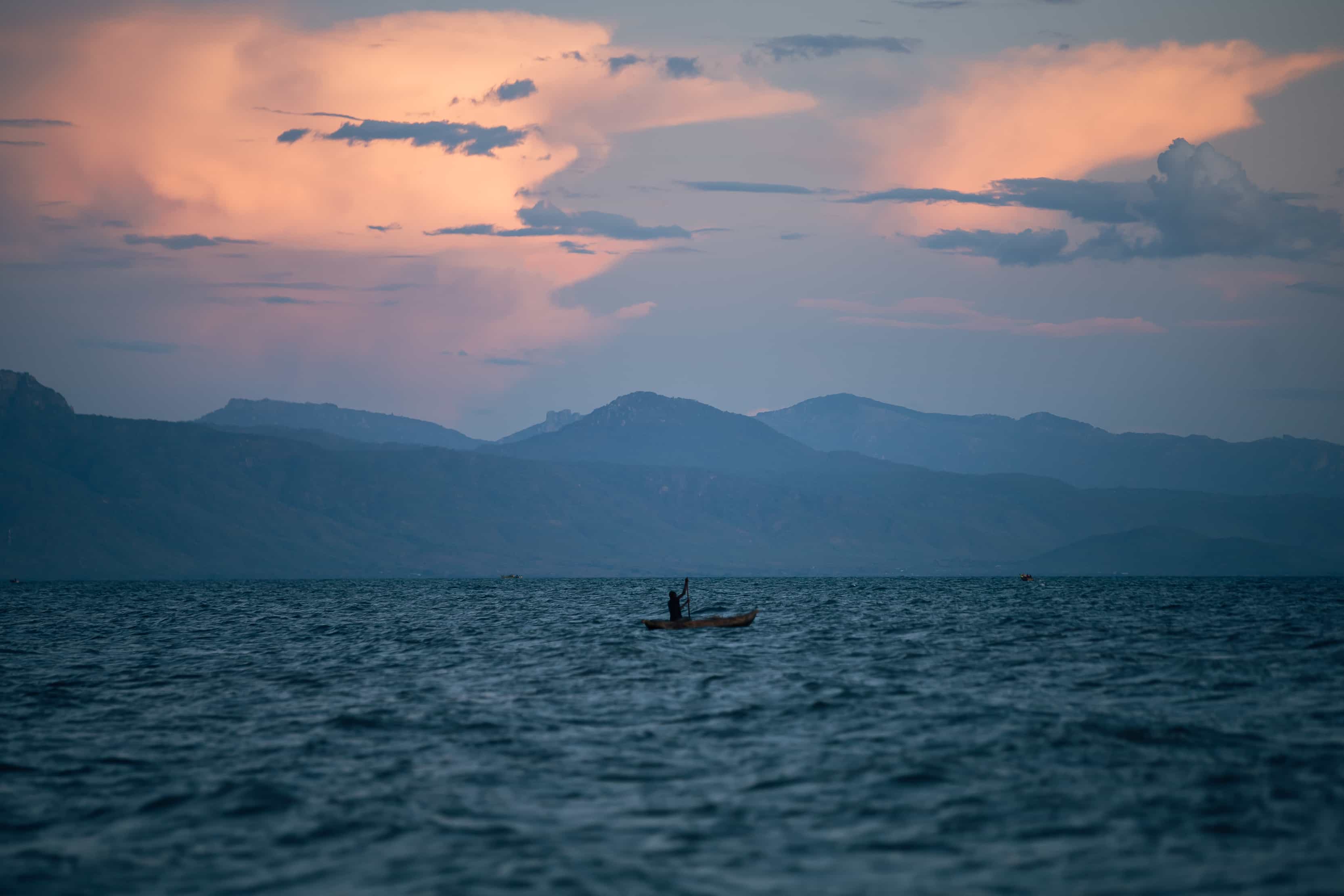 man rowing canoe in lake at sunset