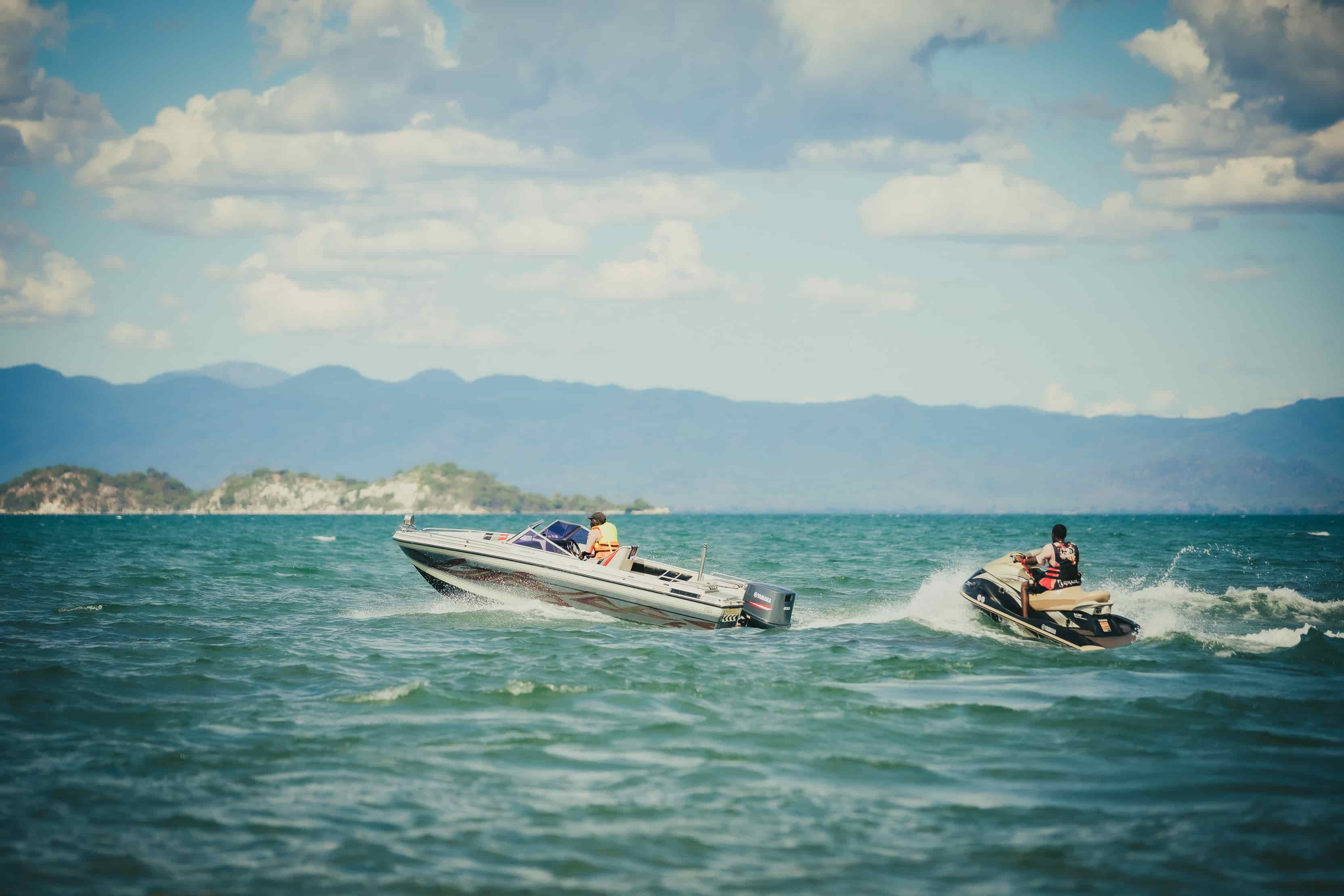 boat cruising on the lake and jetski behind it with island view