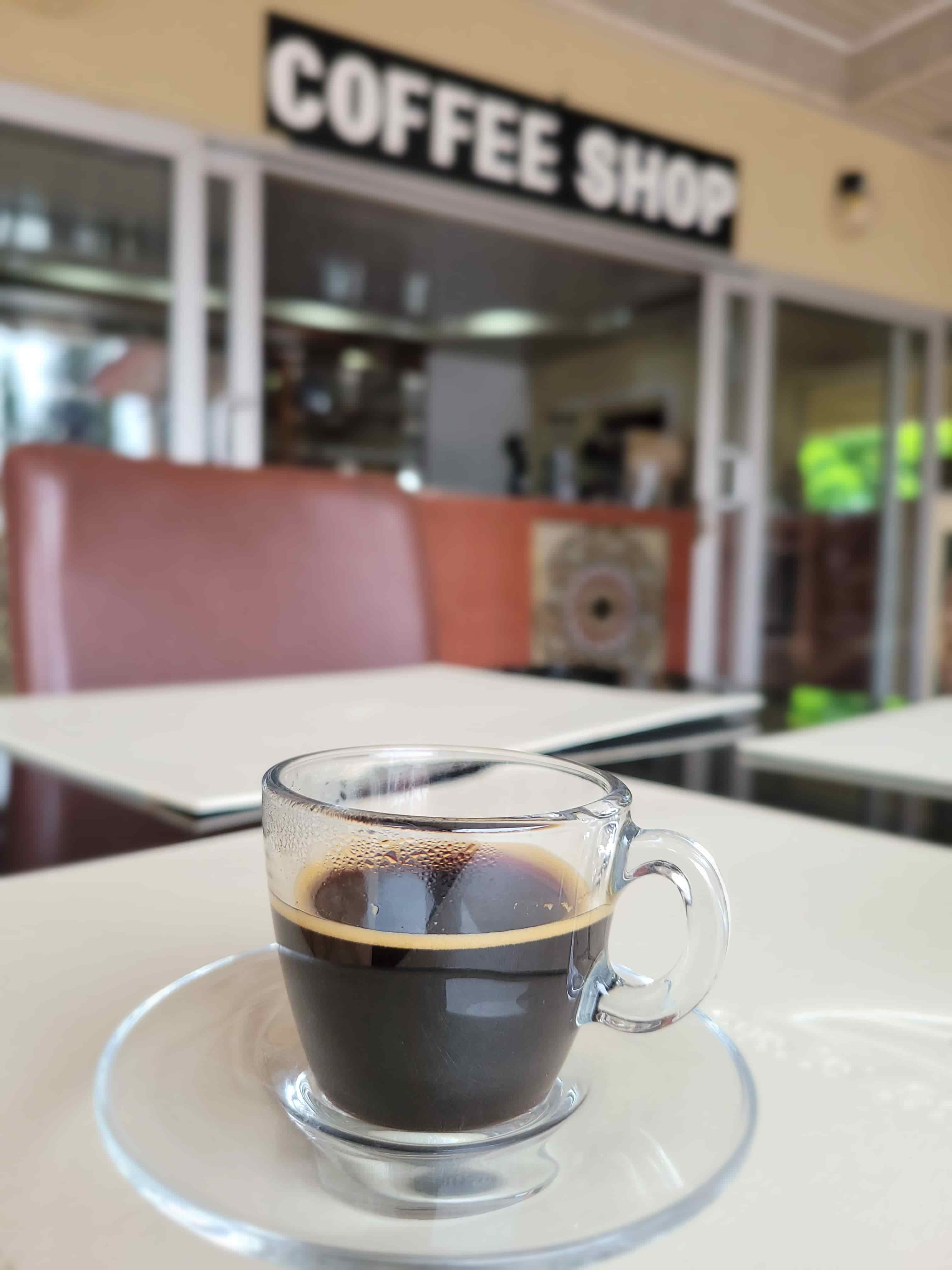close up of espresso outside coffee ontop of table with view of coffee shop and sign